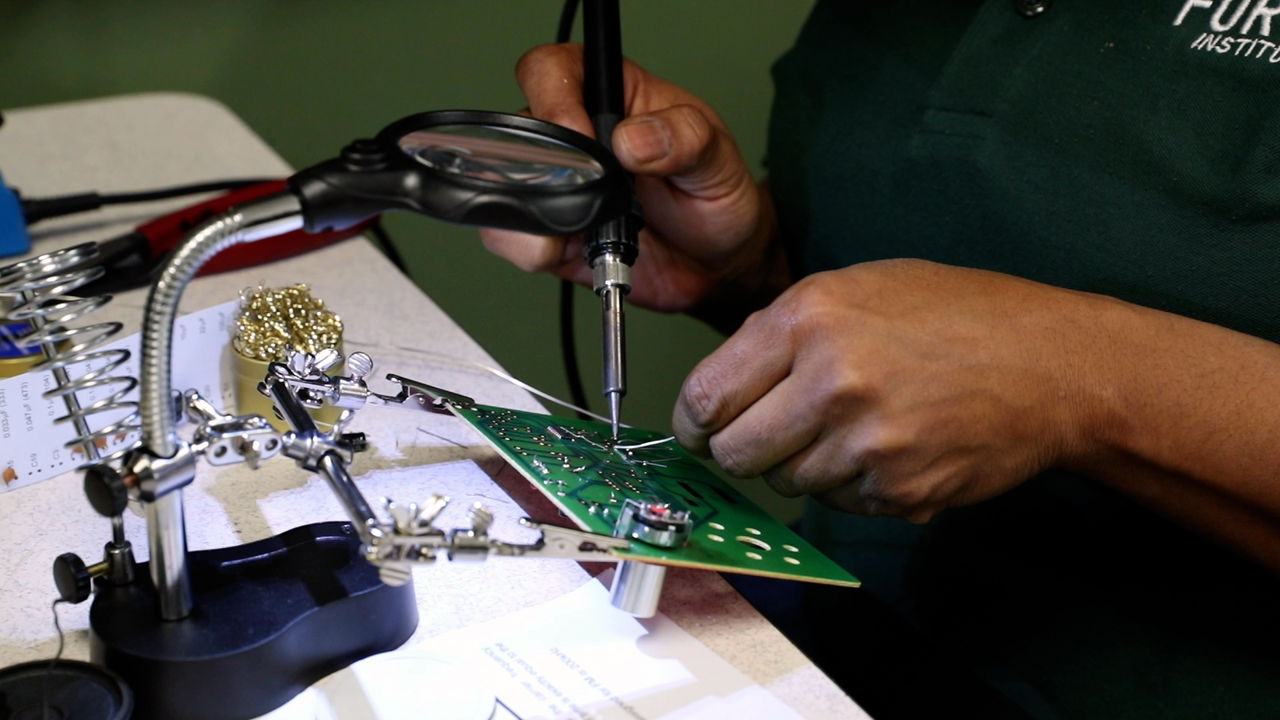 Technician Soldering Circuit Board with Magnifying Glass